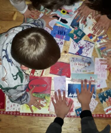 cartoline di natale messe in ordine per formare la sagoma di un albero di natale, contornate dalle mani di bambini/e