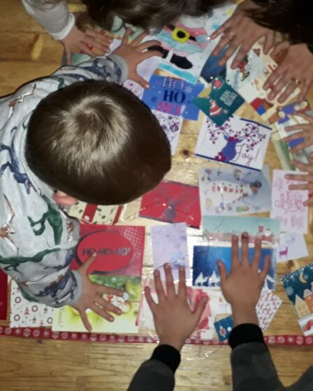 cartoline di natale messe in ordine per formare la sagoma di un albero di natale, contornate dalle mani di bambini/e