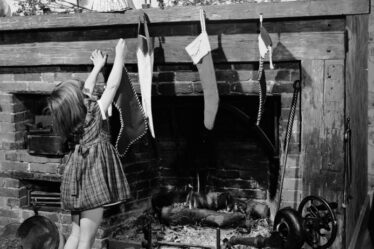 In una foto in bianco e nero una bambina sta finendo di appendere le calze al caminetto.