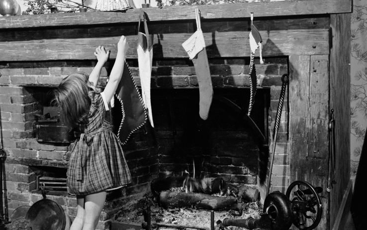 In una foto in bianco e nero una bambina sta finendo di appendere le calze al caminetto.