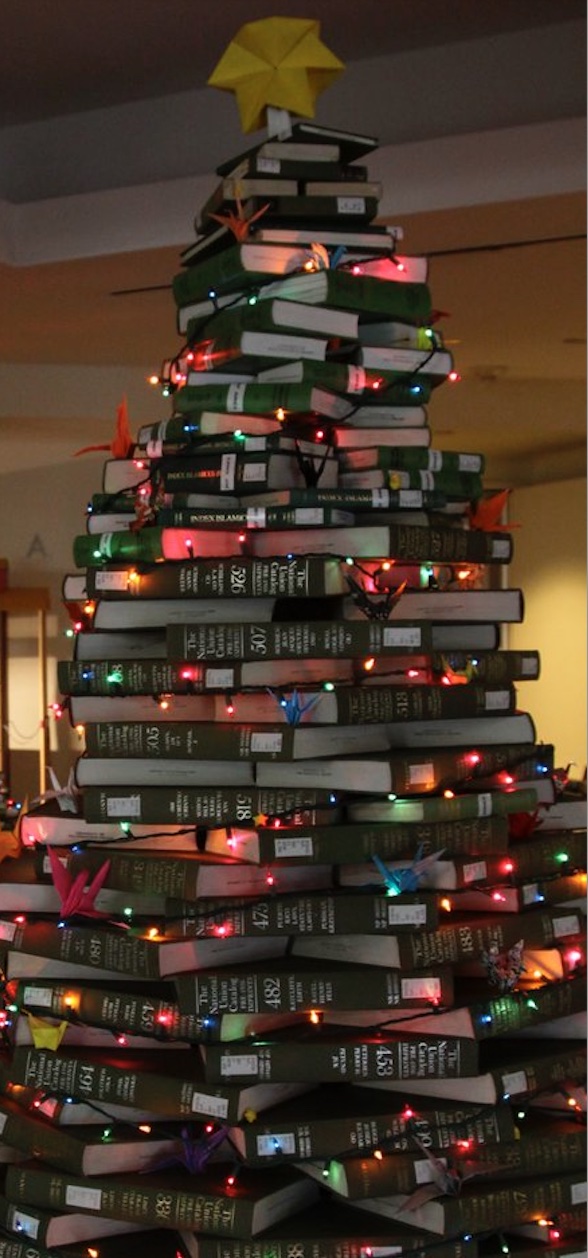 Albero di natale formato da libri impilati tra loro a formare un'abete, contornato da lucine.